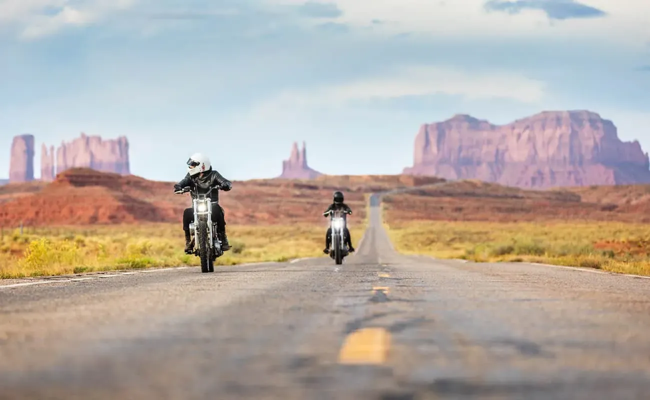 A rider on a Harley-Davidson Road Glide cruising down an American desert highway heading towards a Formula 1 race