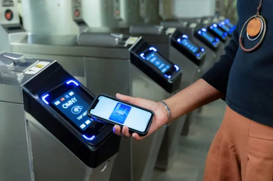 A traveler tapping their credit card on an OMNY reader at the JFK AirTrain exit turnstiles at Jamaica Station