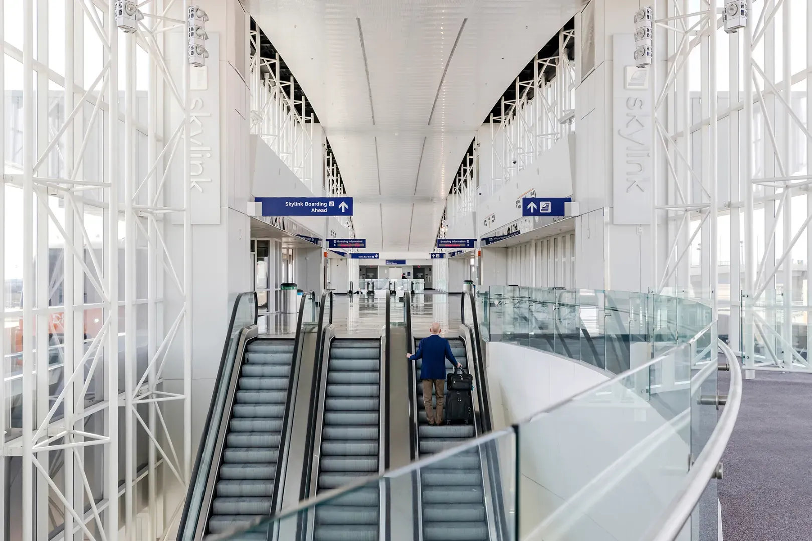 Overhead directional signs inside a DFW terminal pointing passengers to the Skylink escalator