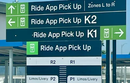 Green signs directing passengers to the designated Uber and Lyft Ride App pickup zones at JFK