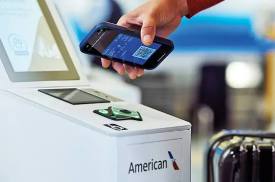 A traveler checking in luggage at an airport kiosk paying the new $50 domestic baggage fees for American, Delta, and United